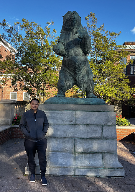 Stallone Kohia, MMed stands with his arms inside of a dark jacket in front of the green-tinged “Bronze Bruno” statue.