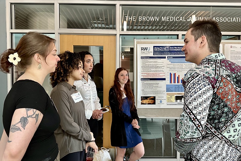 A group of students speak in front of a research poster in the atrium of The Warren Alpert Medical School.